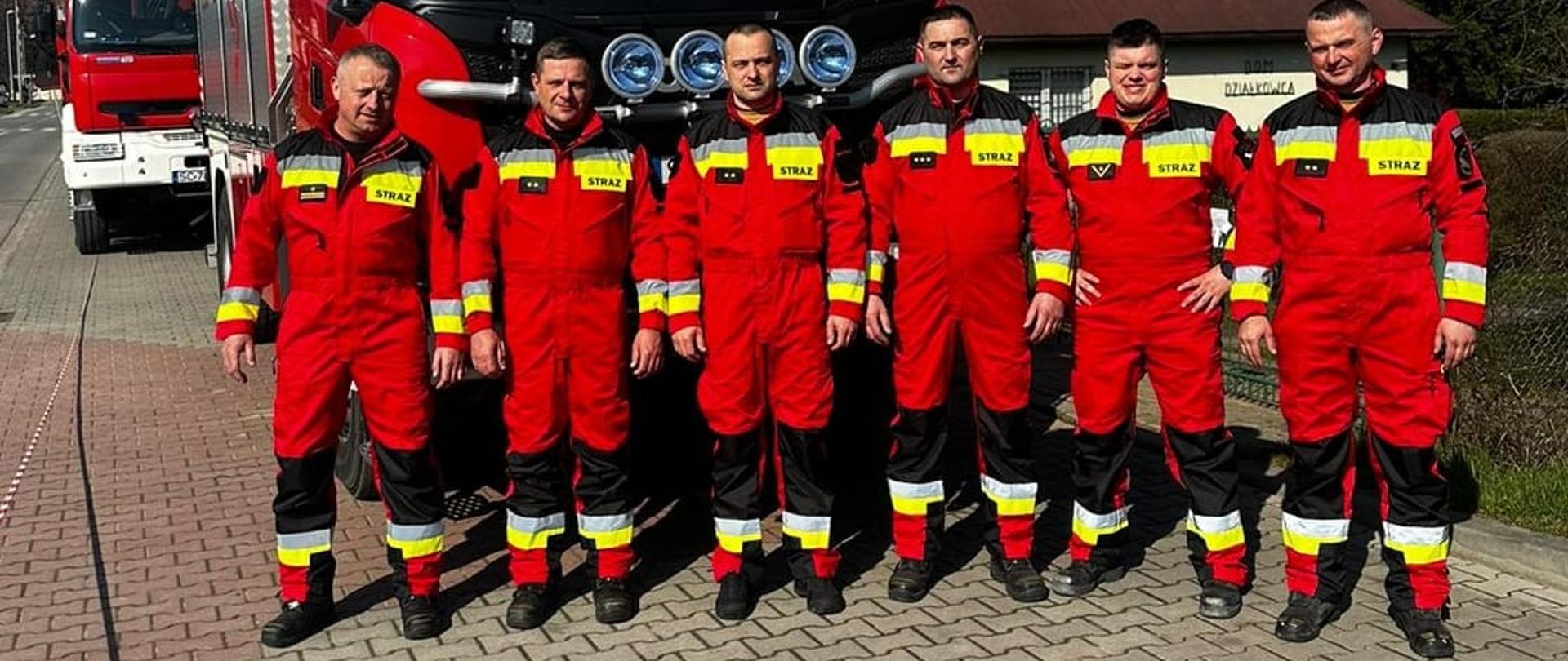 Sześciu strażaków stojących na tle samochodu pożarniczego