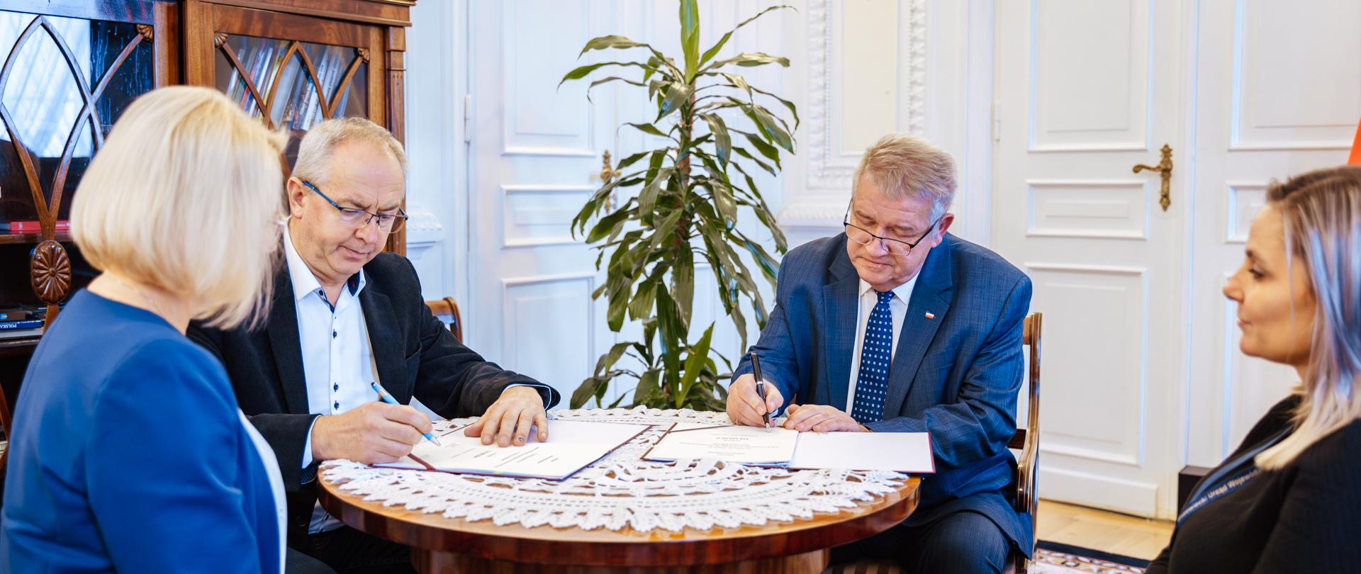 Przy stole siedzą cztery osoby. Podpisują umowę na zakup. 