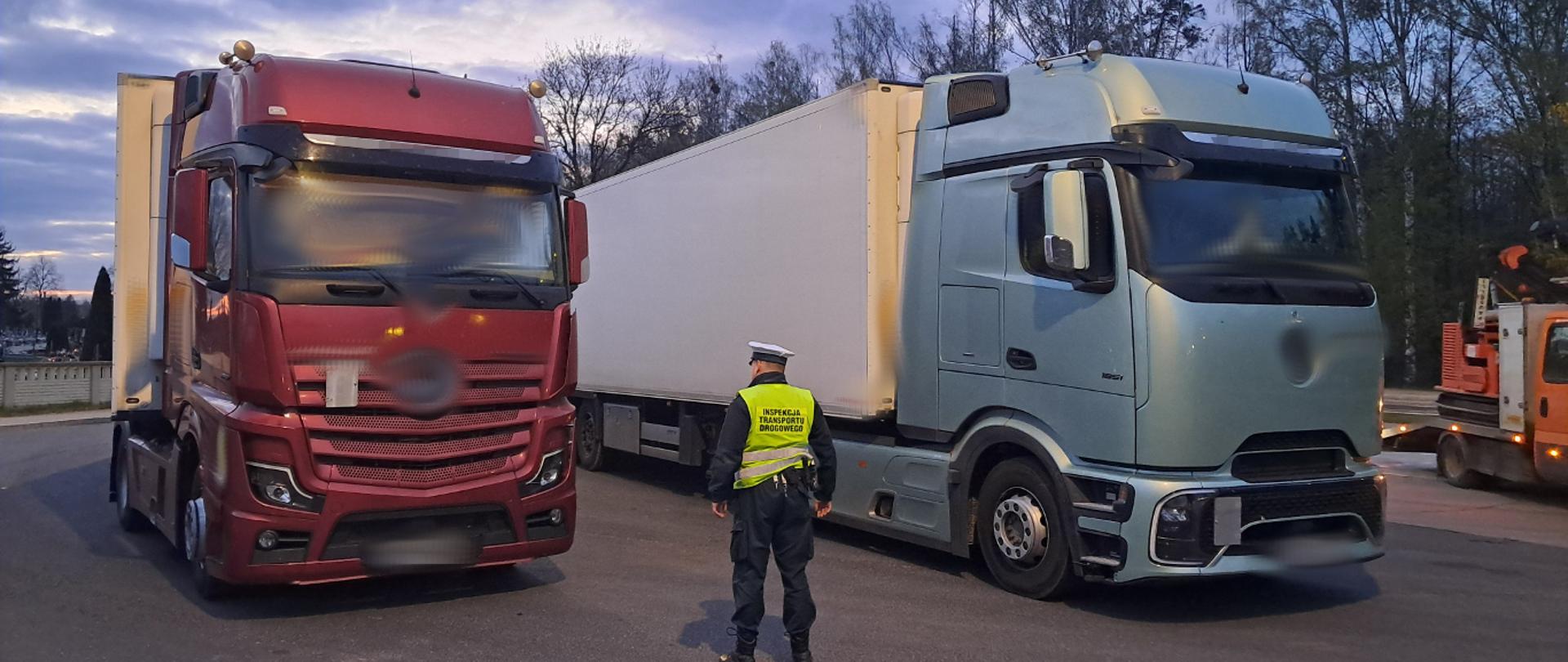 Inspektor w kamizelce odblaskowej stoi przed dwiema ciężarówkami z kontenerami chłodniczymi