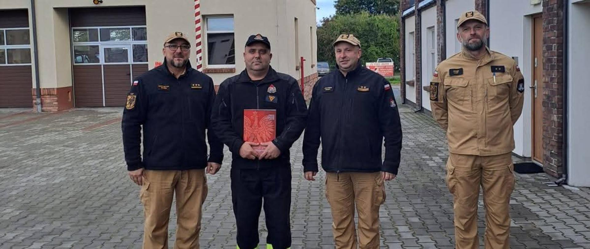 Na zdjęciu Komendanci, Zastępca Dowódcy JRG oraz nagrodzony funkcjonariusz st. ogn. Adam Bisewski. Funkcjonariusze są ubrani w stroje koszarowe. 