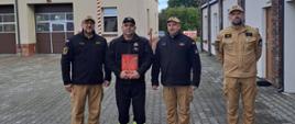 Na zdjęciu Komendanci, Zastępca Dowódcy JRG oraz nagrodzony funkcjonariusz st. ogn. Adam Bisewski. Funkcjonariusze są ubrani w stroje koszarowe. 