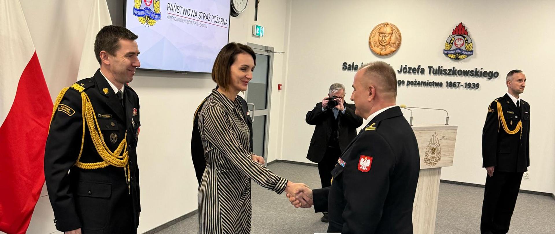 duża sala, kobieta (wojewoda ) podaje rękę mężczyźnie (nowy komendant), 