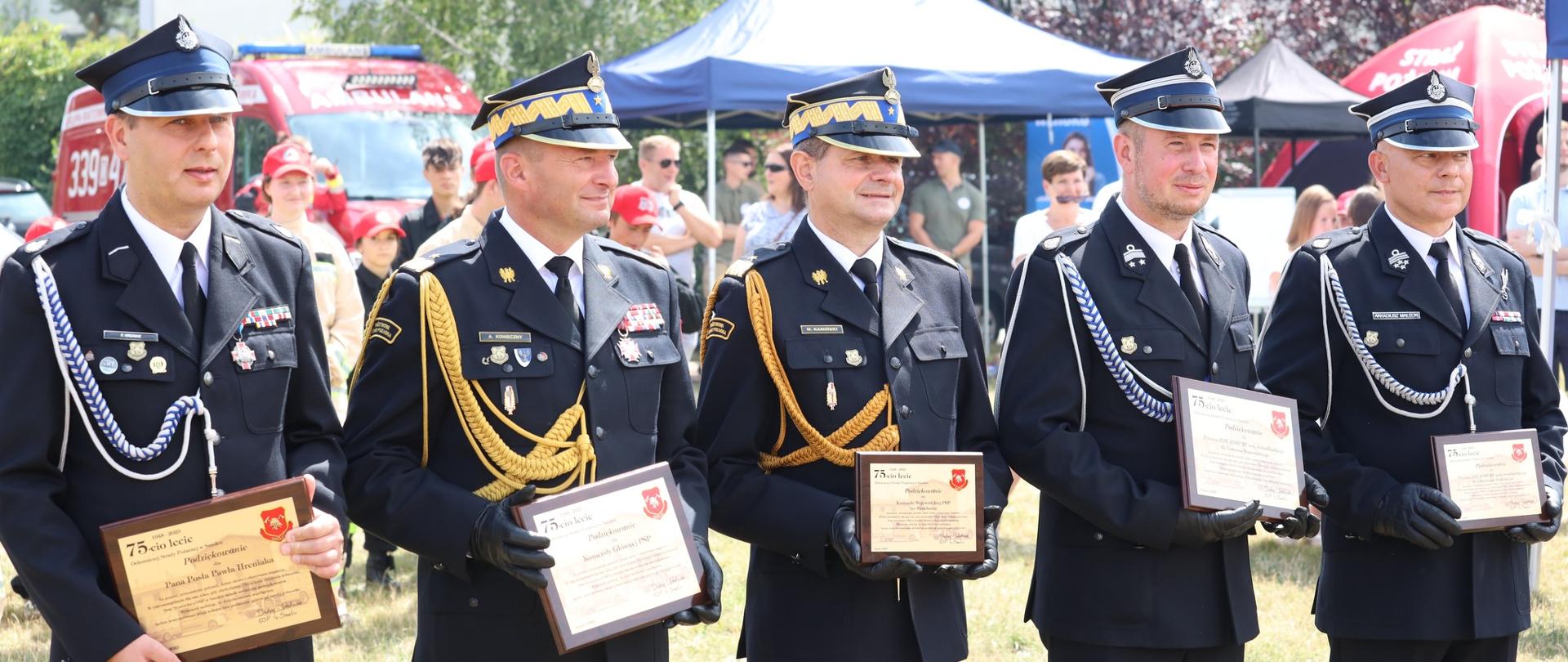 Strażacy Państwowej Straży Pożarnej oraz druhowie Ochotniczych Straży Pożarnej trzymający drewniane wyróżnienia.