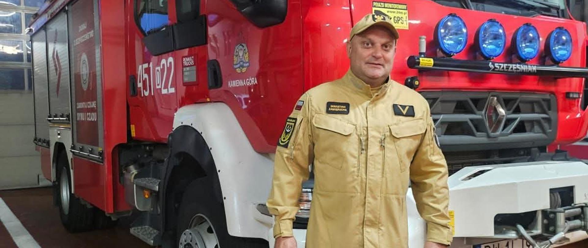 ogn. Sebastian Zawierucha strażak ustawiony na tle pojazdu ratowniczo gaśniczego. Zdjęcie wykonane w garażu jednostki