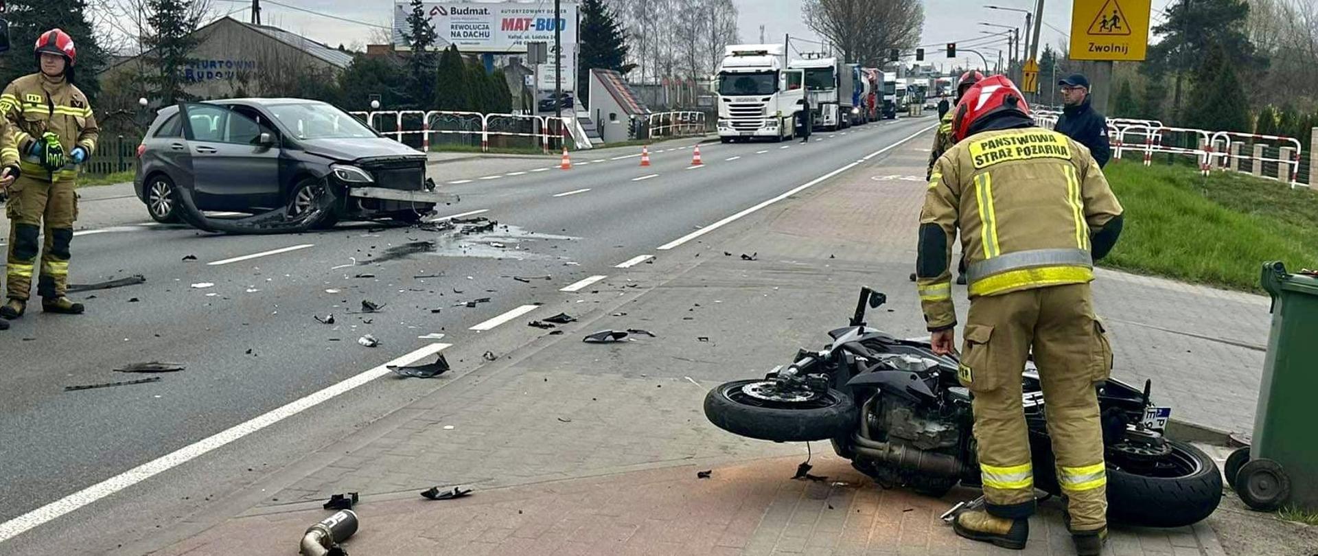 Strażak pochylony nad uszkodzonym motocyklem w tle uszkodzony samochód.