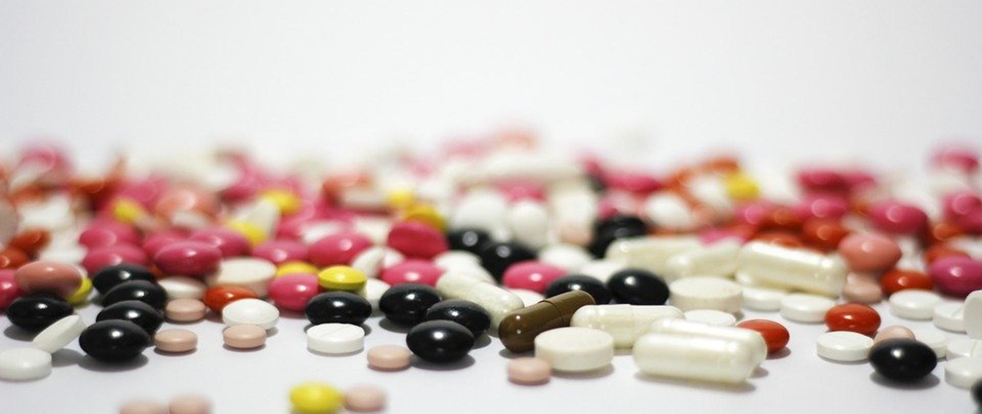 różnokolorowe tabletki rozsypane na białym blacie.