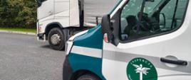 Na pierwszym planie inspekcyjny furgon, na drugim planie biała kabina ciężarówki. Pojazdy stoją na przydrożnym parkingu.