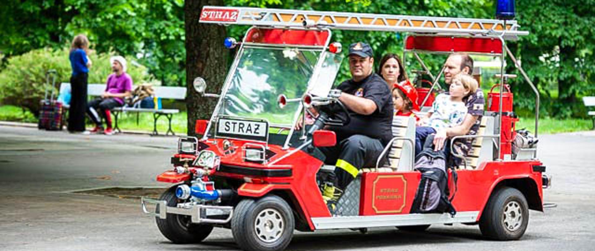 Na zdjęciu widać rodzinę z dziećmi oraz strażaka jadących melexem stylizowanym na wóz strażacki.