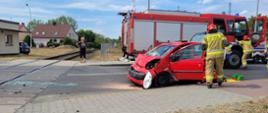 Przed przejazdem kolejowym w Żarach na ulicy Moniuszki doszło do zderzenia czołowego samochodów osobowych. Na zdjęciu widać jeden samochód osobowy marki citroen c1 koloru czerwonego z rozbitym przodem pojazdu. Strażacy udzielają pierwszej pomocy przedmedycznej osobie poszkodowanej w citroenie.