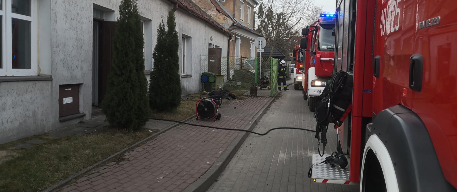 Zdjęcie przedstawia zastępu pożarnicze ustawione równolegle do zagrożonego obiektu, w którym prowadzone są działania gaśnicze.