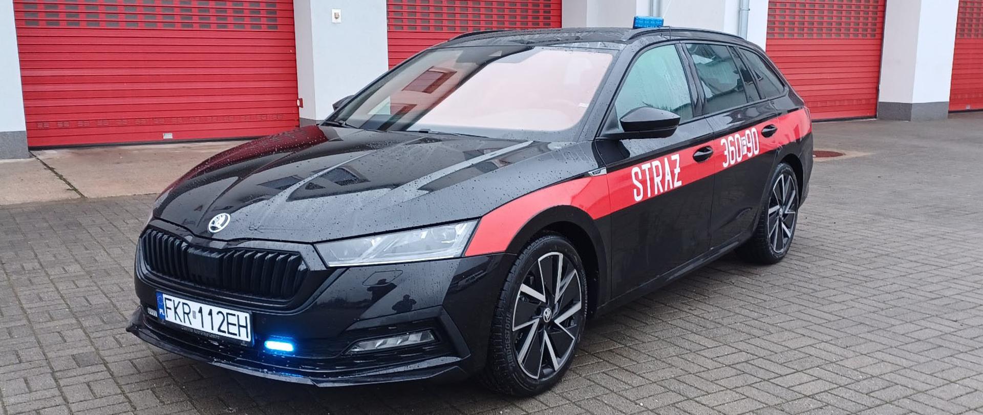 Na zdjęciu widoczny jest pojazd Skoda Octavia koloru czarnego z czerwonym pasem z napisem "Straż".