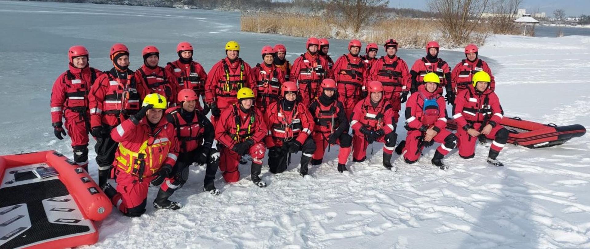 Strażacy Państwowej Straży Pożarnej w ubraniach wypornościowych i kaskach stoją na brzegu do wspólnego zdjęcia grupowego.