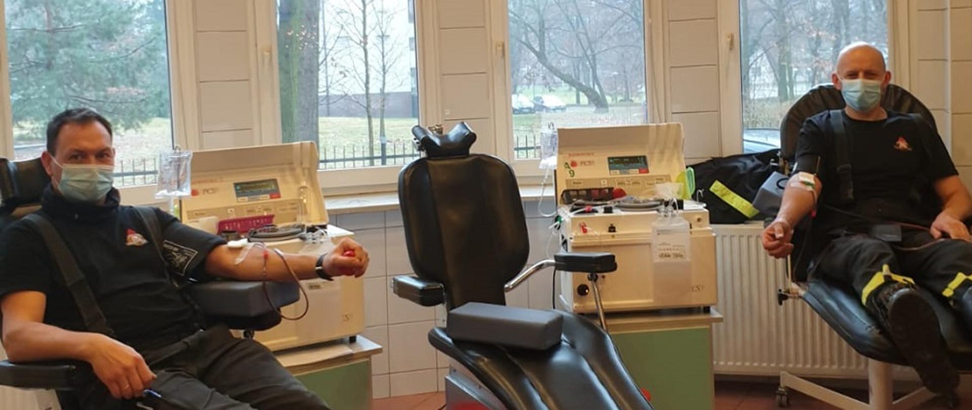 Zdjęcie zrobione wewnątrz budynku Regionalnego Centrum Krwiodawstwa i Krwiolecznictwa Oddział Terenowy w Rybniku. Dwóch strażaków ubranych w ubrania koszarowe siedzi w fotelach i oddaje osocze