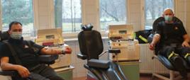 Zdjęcie zrobione wewnątrz budynku Regionalnego Centrum Krwiodawstwa i Krwiolecznictwa Oddział Terenowy w Rybniku. Dwóch strażaków ubranych w ubrania koszarowe siedzi w fotelach i oddaje osocze
