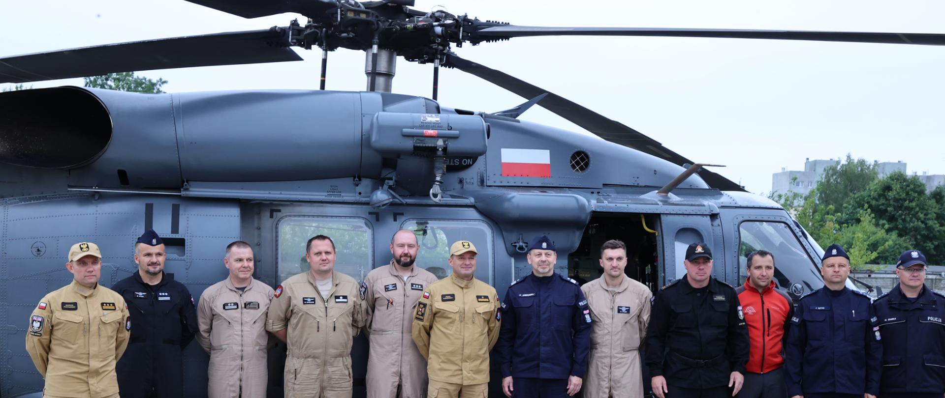 Na płycie lotniska na tle śmigłowca policyjnego pozują do zdjęcia strażacy i policjanci