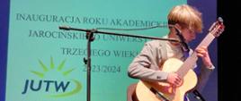 Zdjęcie przedstawia ucznia grającego na gitarze podczas koncertu dla UTW w Jarocinie.