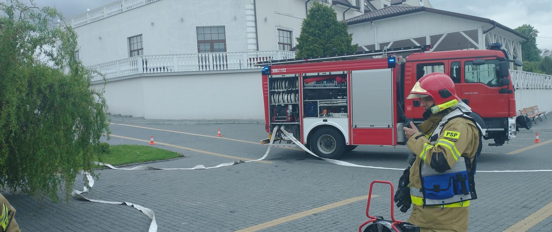 Zdjęcie przedstawia samochód gaśniczy oraz rozwinięta linię główną. Kierujący Działaniem Ratowniczym prowadzi korespondencję radiową
