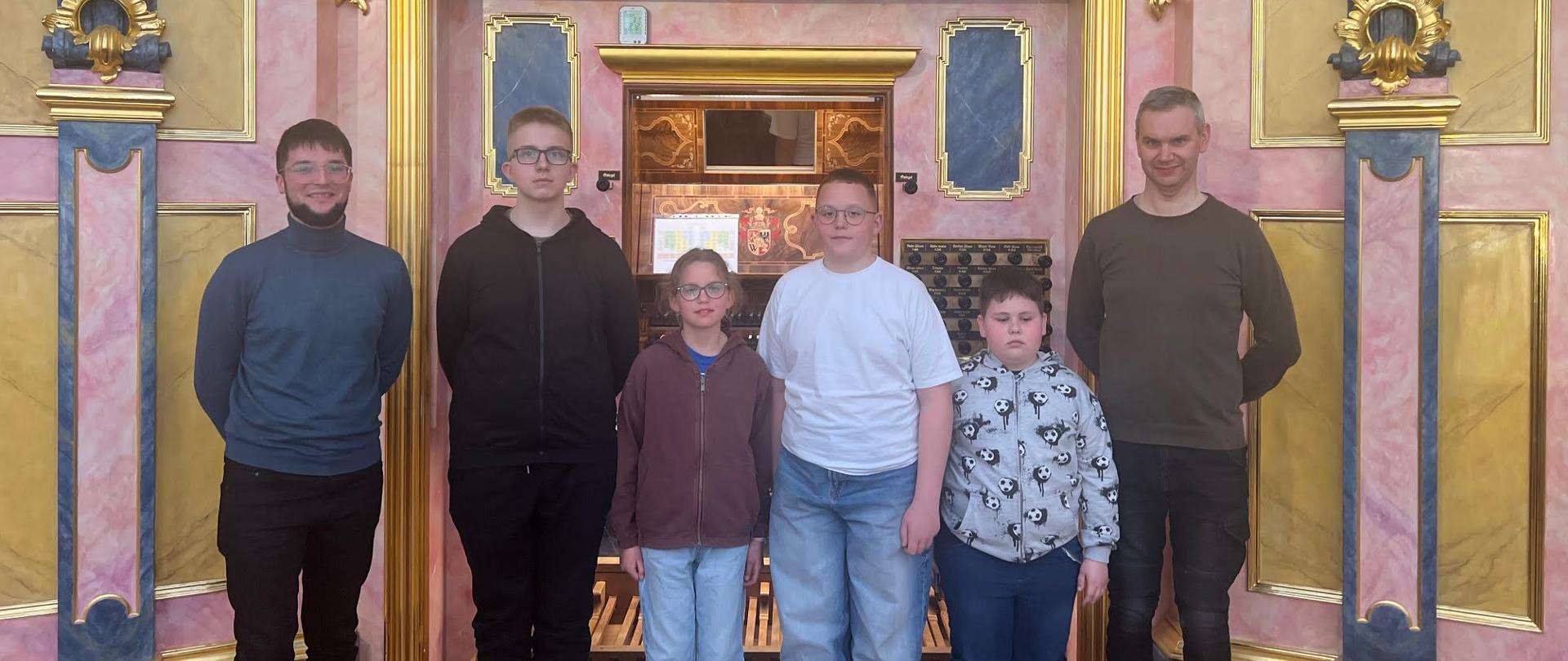 Pięć osób stojących na tle organów kościelnych.