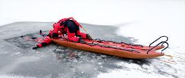 Zdjęcie przedstawia strażaka-ratownika znajdującego się na saniach lodowych, który
wyjmuje innego strażaka z przerębla.