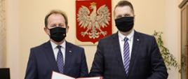 Prof. Bernacki i minister Czarnek stoją obok siebie, , prof. Bernacki trzyma nominację, za nimi na ścianie godło Polski.