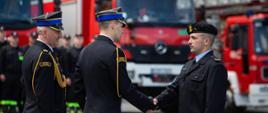 Na zdjęciu widoczni komendant Powiatowy PSP w Gorlicach z zastępcą wręczający strażakowi awans na wyższy stopień służbowy. Komendanci w galowych granatowych mundurach i w czapkach rogatywce. Strażak odbierający awans w ubraniu granatowym służbowym i berecie.
