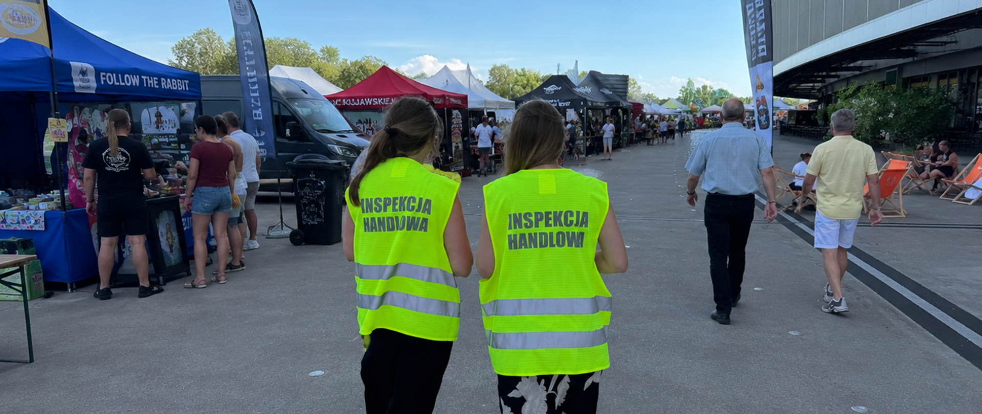 Na pierwszym planie dwie inspektorki Inspekcji Handlowej. W tle namioty przedsiębiorców rozstawione na płycie przy stadionie w trakcie festiwalu.