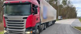 Na pierwszym planie (od lewej): przód i lewy bok kontrolowanego ciągnika siodłowego z podpiętą naczepą. W tle: oznakowany furgon zachodniopomorskiej Inspekcji Transportu Drogowego stoi w zatoce kontrolnej przy krajowej „dziesiątce”.