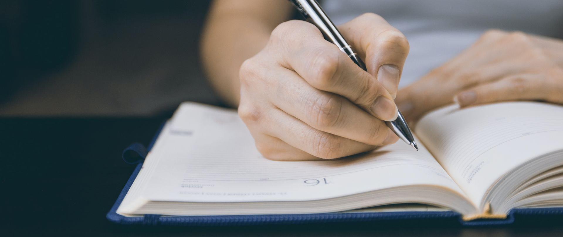 Dłoń z długopisem oparta o notatnik.