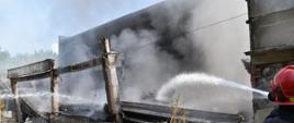 Dogaszanie hali o konstrukcji żelbetowej, dach zawalony. Widać unoszący się biały dym Z prawej strony strażak podaje jeden prąd wody w natarciu do wnętrza hali.