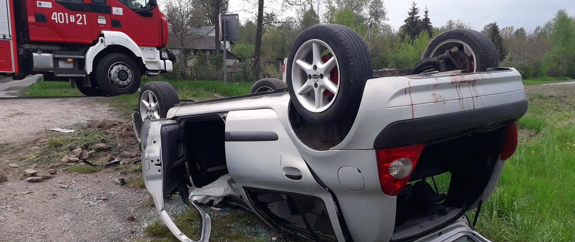 Zdjęcie przedstawia przewrócony samochód osobowy koloru srebrnego.