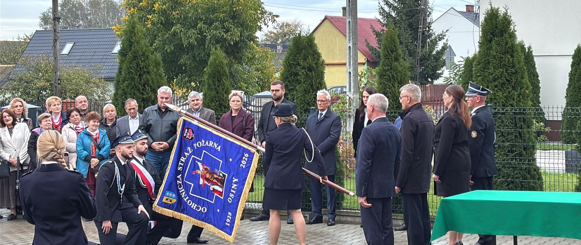 Druhowie OSP Osiny, odbierają sztandar , w tle zaproszeni koście