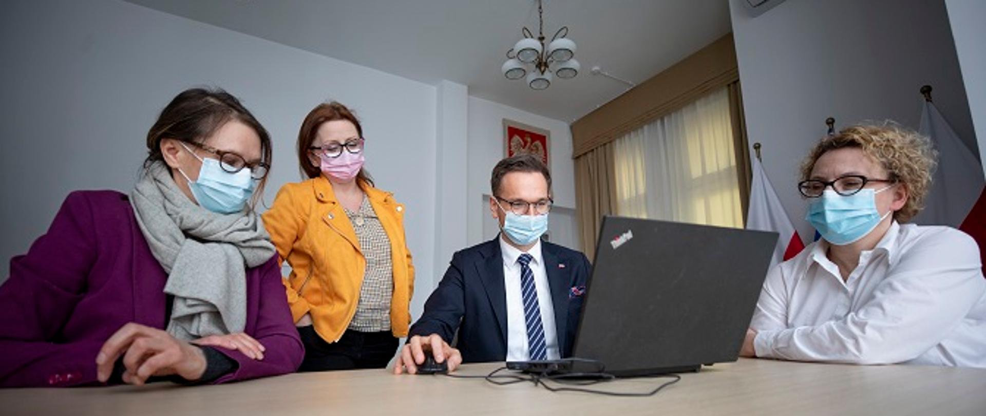Wiceminister Waldemar Buda siedzi przed laptopem w swoim gabinecie. Towarzyszą mu trzy pracownice MFiPR.