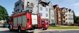 Samochód straży pożarnej stojący przed szeregiem połączonych budynków mieszkalnych