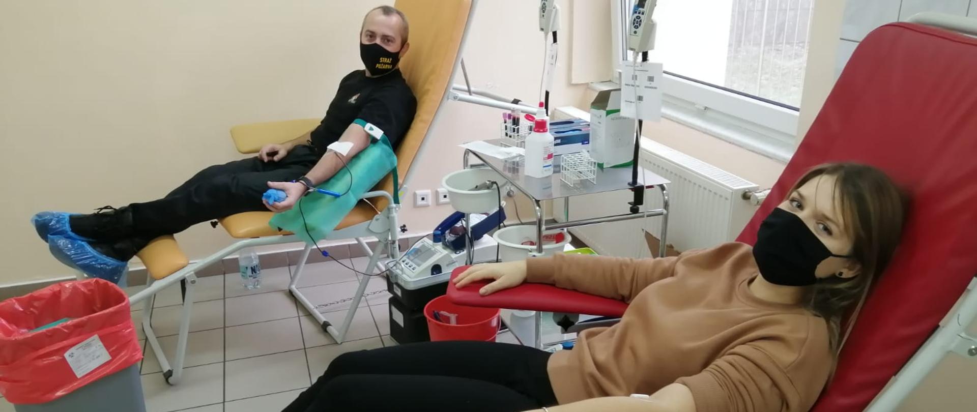 Na zdjęciu znajdują się dwie osoby w fotelach służących do pobierania krwi. Po lewej stronie znajduje się Komendant Powiatowy PSP, który oddaje krew, po lewej stronie kobieta, która jest już po oddaniu krwi.