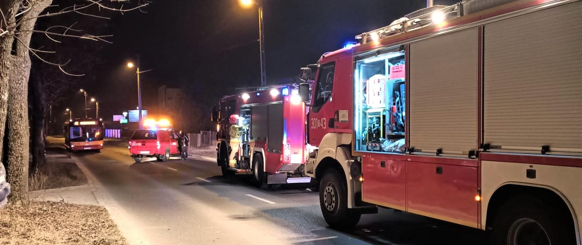 Na zdjęciu przedstawiono stojące wzdłuż ulicy 3 samochody pożarnicze biorące udział w zdarzeniu. Na drugim pasie stoi autobus miejski.