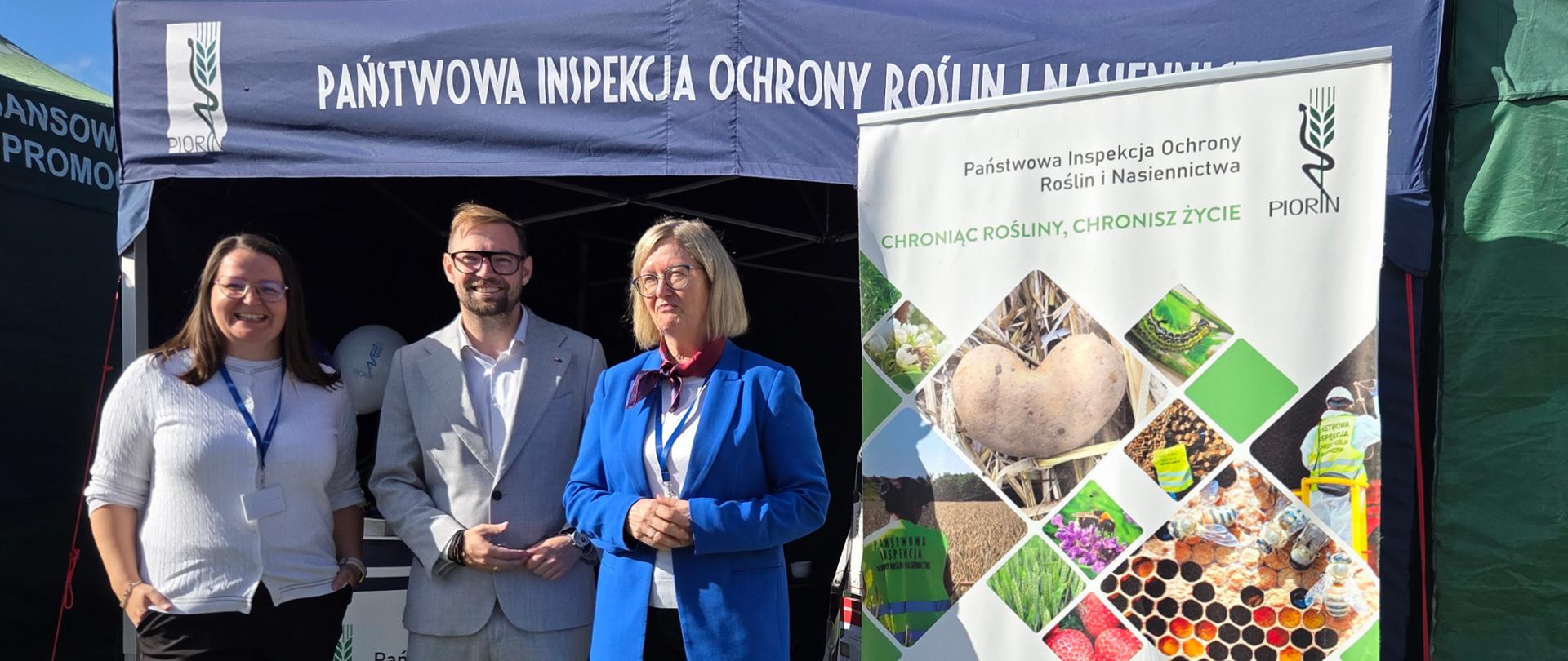 Dwie kobiety i mężczyzna stoją uśmiechnięci przy namiocie 