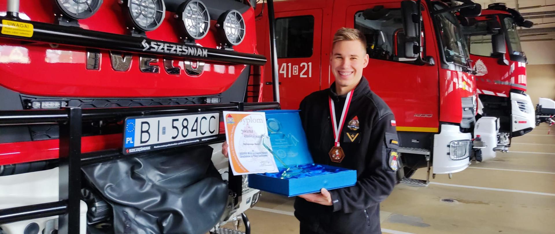 Strażak na tle samochodów pożarniczych z nagrodą za najlepszego libero