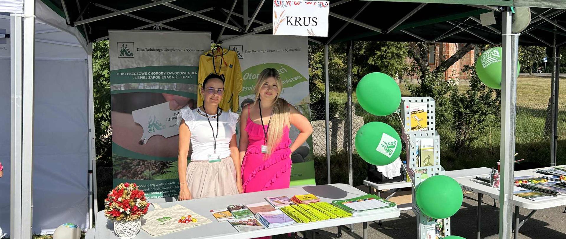 Przy stoisku informacyjno-prewencyjnym Kasy znajdują się 2 osoby – pracownice placówki. Przed mini znajduje się stół, na którym wyłożone są materiały prewencyjne Kasy (ulotki, odblaski, plany lekcji dla dzieci).