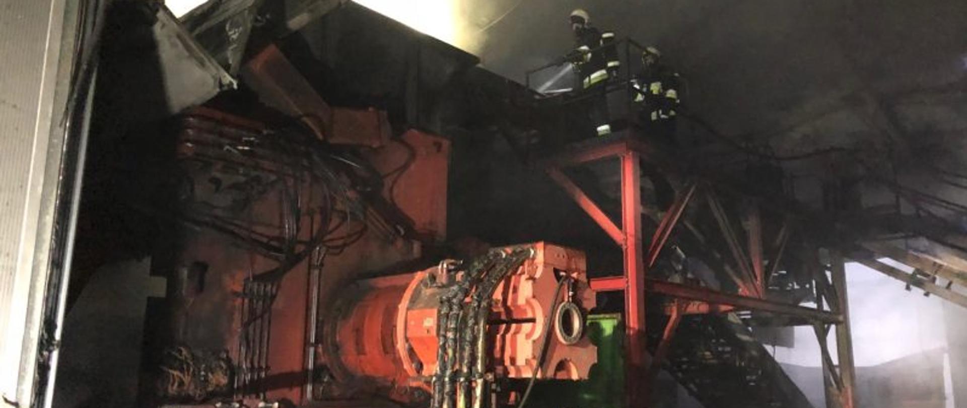 Strażacy gaszący pożar maszyny od której zaczął się pożar w sortowni śmieci 