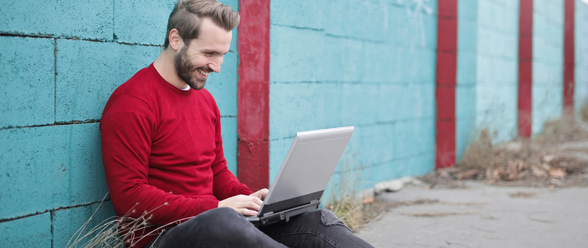 Mężczyzna siedzi na ziemi z laptopem na kolanach.