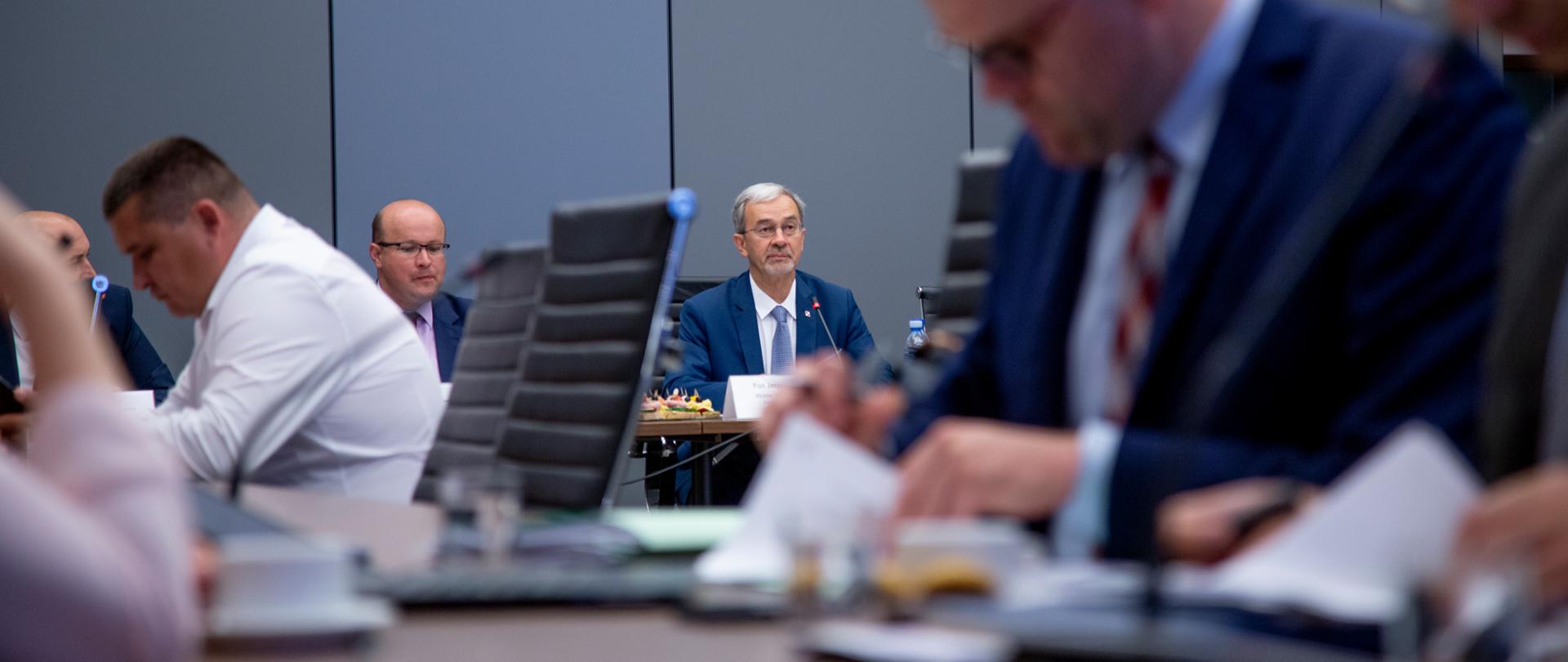 Na zdjęciu sala konferencyjna, na pierwszym planie stół, przy nim siedzą uczestnicy spotkania, w tle stół prezydialny, przy nim siedzi minister Kwieciński.