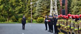 Na pierwszym olania z-ca Komendanta Powiatowego PSP w Ropczycach, po prawej w szyku stoją; strażacy w umundurowaniu galowym stanowiący poczet flagowy , dalej strażacy w umundurowaniu bojowym