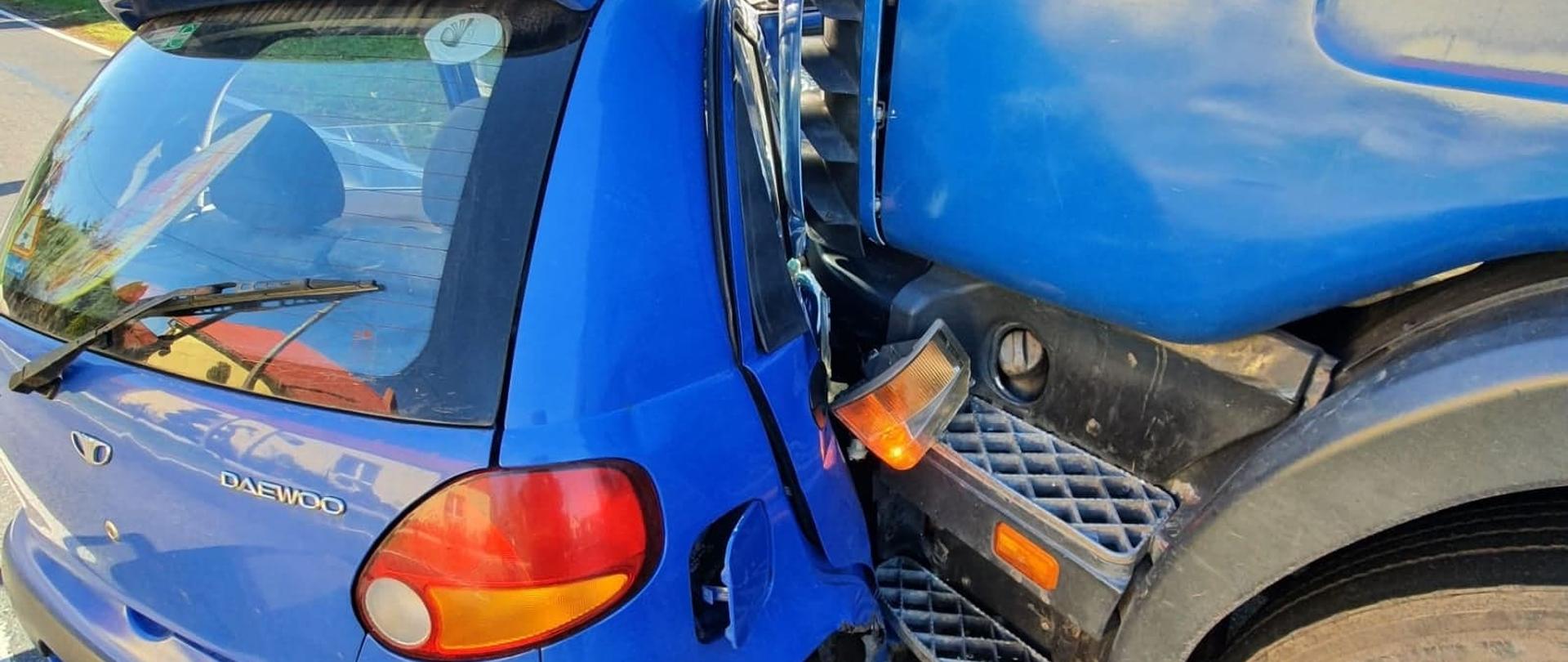 Wypadek drogowy. Wodniki - droga krajowa nr 36. Na głównym planie pojazdy biorące udział w wypadku (stan po zderzeniu): samochód osobowy koloru niebieskiego, stojący w poprzek jednego pasa ruchu, skierowany przodem w stronę pobocza oraz ciągnik siodłowy również koloru niebieskiego stojący na tym samym pasie ruchu, równolegle do osi jezdni. Widoczne są uszkodzenia prawego boku auta, przednia szyba oraz dach. Ciągnik siodłowy z kolei ma uszkodzone lampy z lewej strony. W tle zabudowania, znaki drogowe i drzewa. 