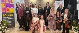 Galeria 17 zdjęć z koncertu klasy skrzypiec p. Krystyny Ślęzak pt. "Majowe nutki", który odbył się 22 maja 2025 w auli PSM w Kłodzku. Młodzi uczniowie grają na skrzypcach w sali koncertowej.