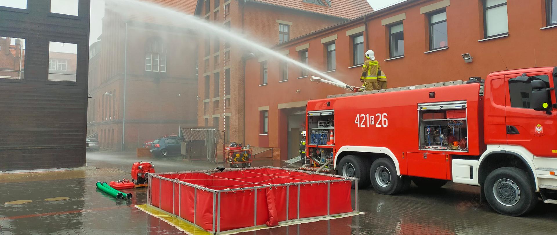 Na zdjęciu widać samochód pożarniczy z którego podawana jest woda z działka. Przy samochodzie rozłożony jest zbiornik wodny