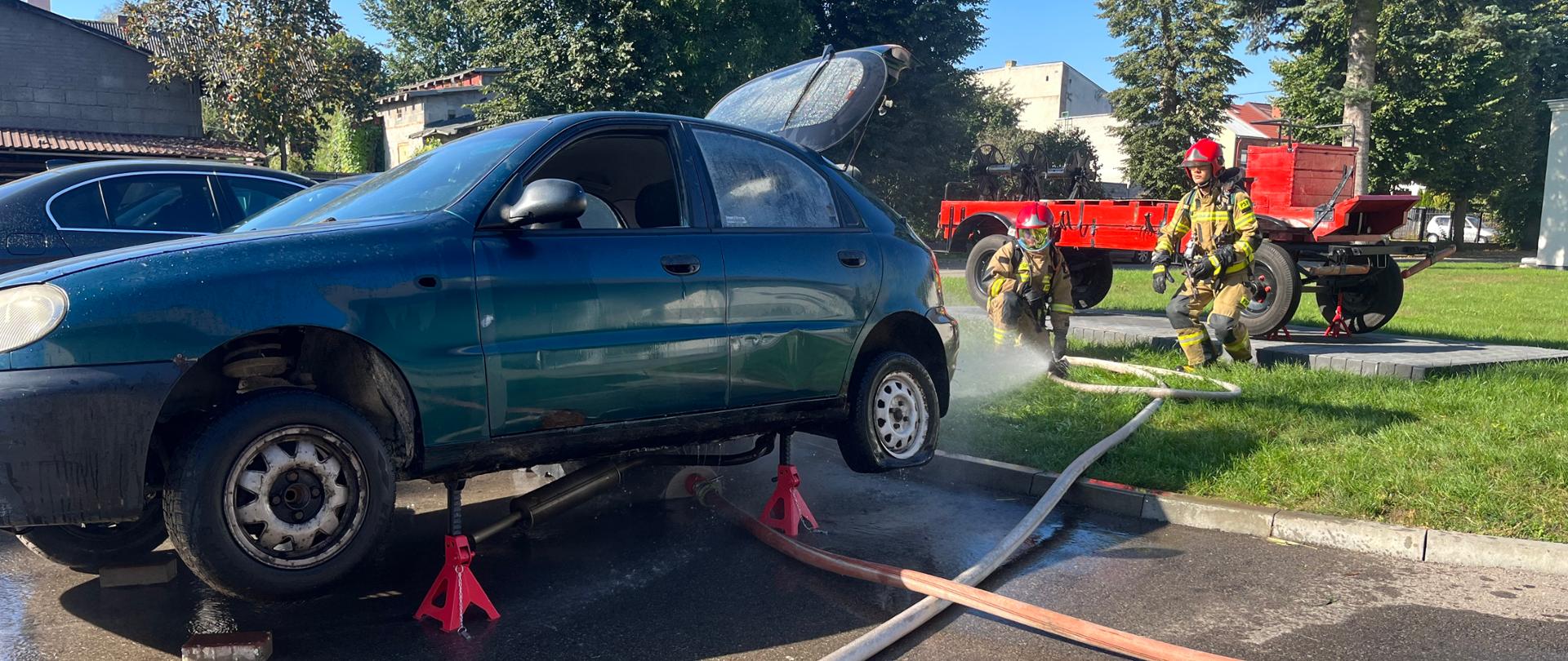 ćwiczenia doskonalące z zakresu ratownictwa technicznego - strażacy gaszą samochód który jest uniesiony na podporach