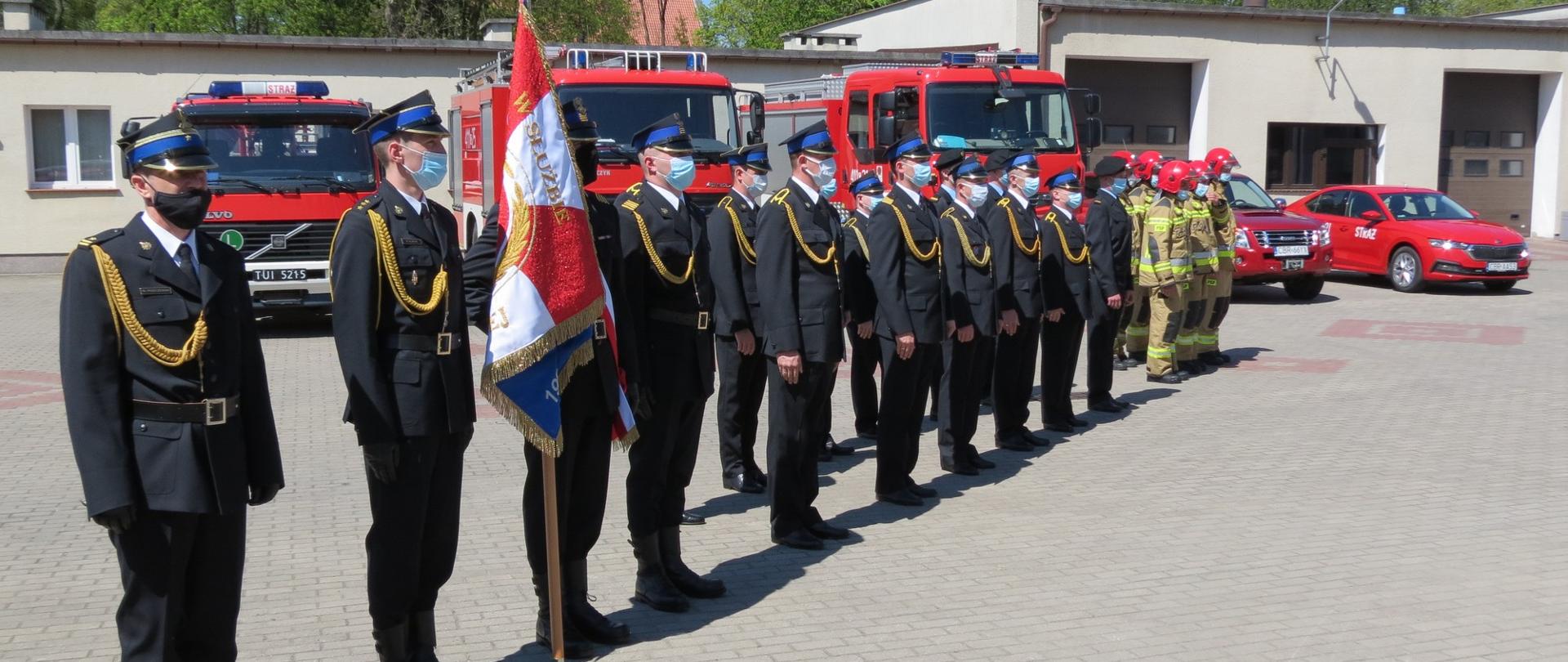 Zdjęcie przedstawia funkcjonariuszy Komendy Powiatowej PSP w Brodnicy podczas uroczystego apelu z okazji Dnia Strażaka. Na pierwszym planie dowódca JRG, oraz poczet sztandarowy, w tle pojazdy Komendy Powiatowej.