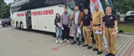 Grupa osób czekająca przed autobusem krwiodawstwa. Troje ubranych w umundurowanie służbowe oraz troje w ubrania prywatne. Autobus stoi przed budynkiem komendy PSP na parkingu 