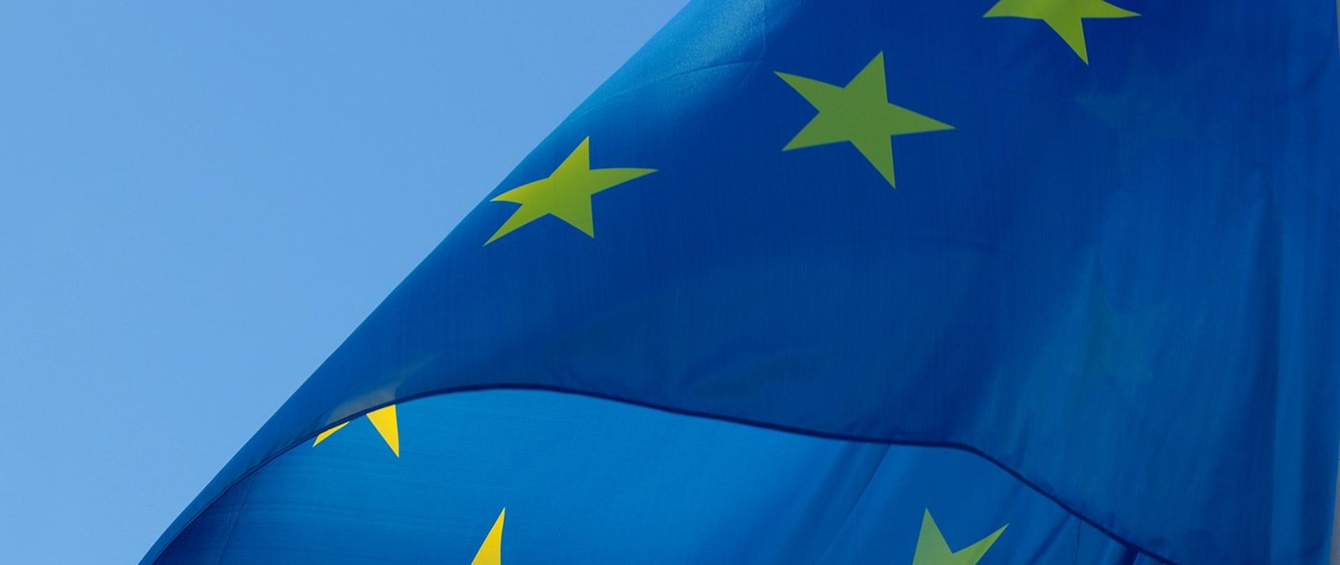 Powiewająca flaga Unii Europejskiej na maszcie - złote gwiazdy na niebieskim tle