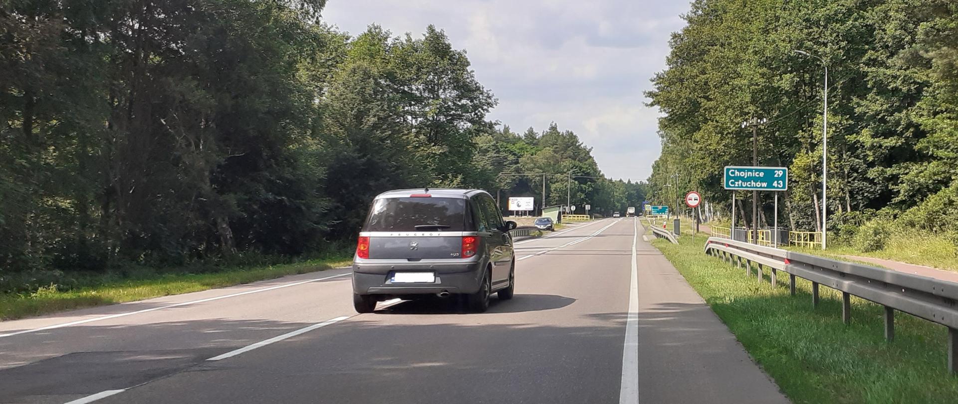 Zdjęcie przedstawia drogę krajową nr 22 między Czerskiem a Chojnicami. Na pierwszym planie jezdnia z samochodem, w oddali znaki drogowe. Wśród znaków tablica drogowskazowa z oznaczeniem odległości do Chojnic i Człuchowa.